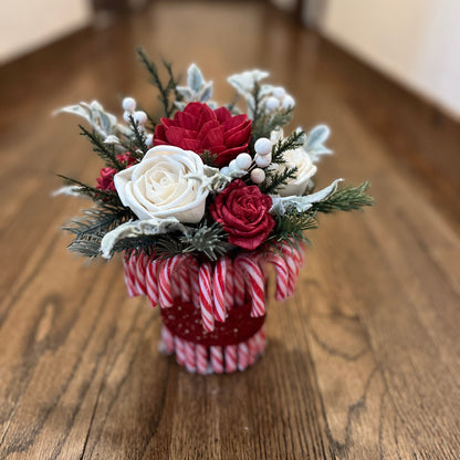Decorative flower arrangement in a candy cane-themed vase on a wooden floor.