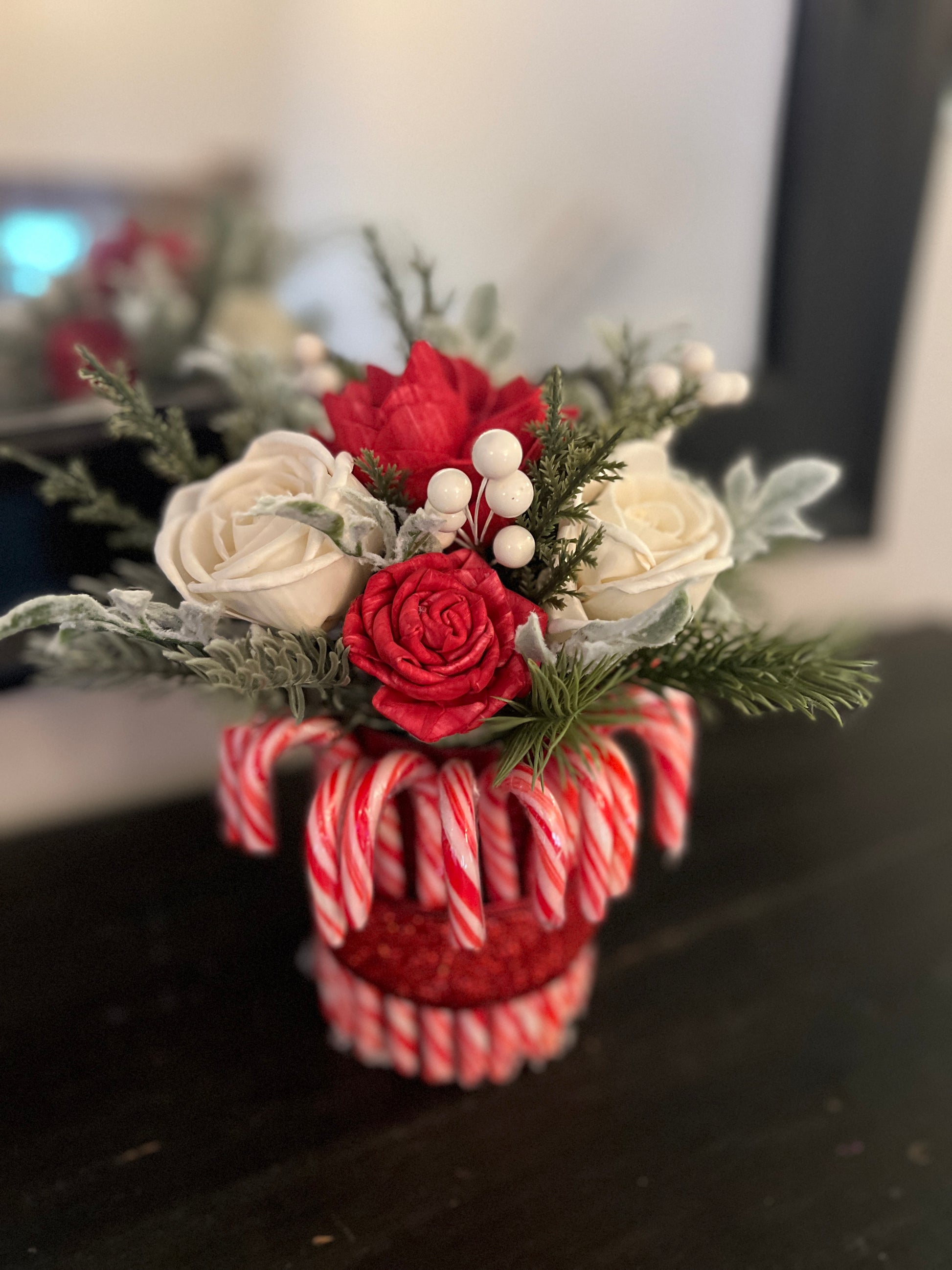 Decorative flower arrangement in a candy cane-themed vase on a dark surface.
